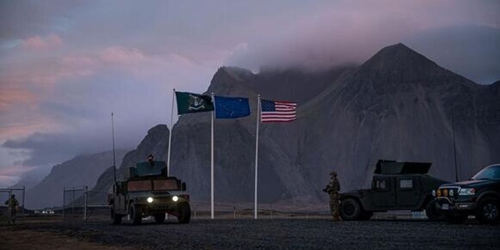 Bidlausschnitt aus dem Film "A House of Dynamite", dunkel gehalten, Militärfahrzeuge auf einer Militärbasis. Unter anderem weht die Europäische und die Amerikanische Flagge.
