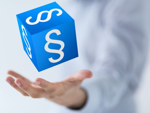Blauer Würfel mit Paragraphen schwebend über einer Hand