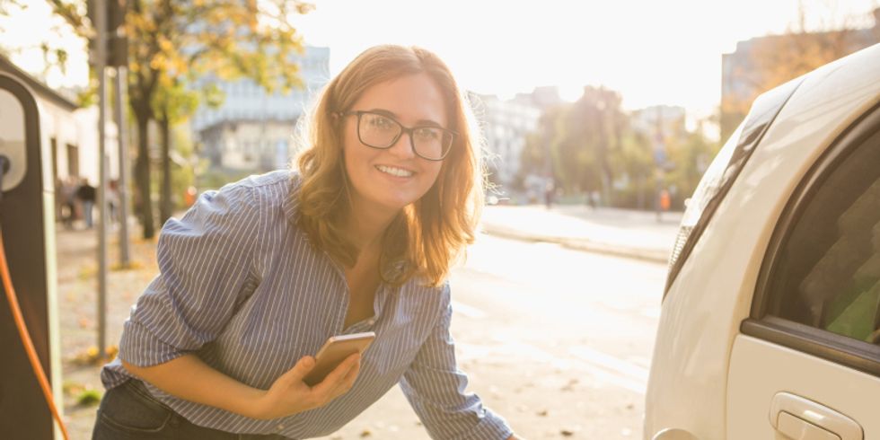 Frau steht am Elektroauto mit Smartphone in der Hand