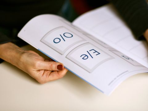 Person blättert durch ein Leerbuch. Eine Hand und eine aufgeschlagene Seite mit den Buchstraben E/e und O/o sind zu sehen.