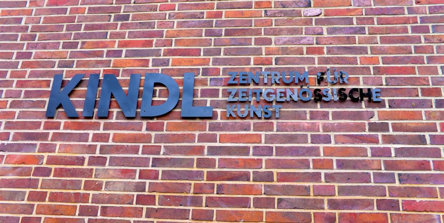 Schriftzug des KINDEl-Zentrums für zeitgenössische Kunst auf dunkelroten Backsteinen. Die einzelnen buchstaben der Schrift sind schwarz. Das Wort "Kindl" ist in größeren Buchstaben geschrieben, als der Rest