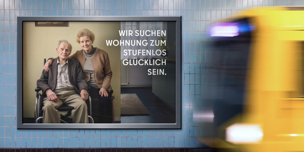 Auf dem Bild ist eine Werbetafel in einer U-Bahn-Station zu sehen. Die Tafel zeigt ein älteres Paar, wobei der Mann im Rollstuhl sitzt. Der Text auf der Tafel lautet: “WIR SUCHEN WOHNUNG ZUM STUFENLOS GLÜCKLICH SEIN.” Im Hintergrund bewegt sich ein Zug.