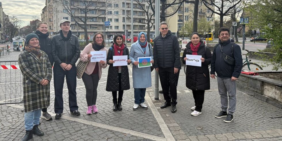 Neun Personen stehen nebeneinander vor einem Fahnenmast.