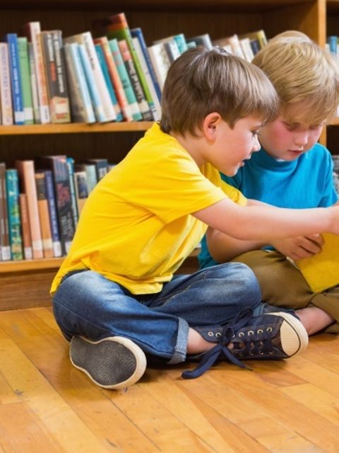 zwei Jungs sitzen vor einem Bücherregal und lesen in einem Buch