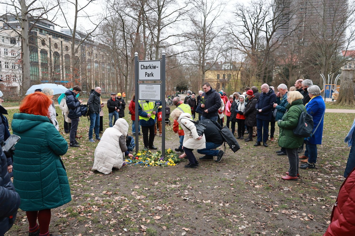 24. Februar 2023: Menschen legen gelbe Rosen am Schild des Charkiw-Parks nieder