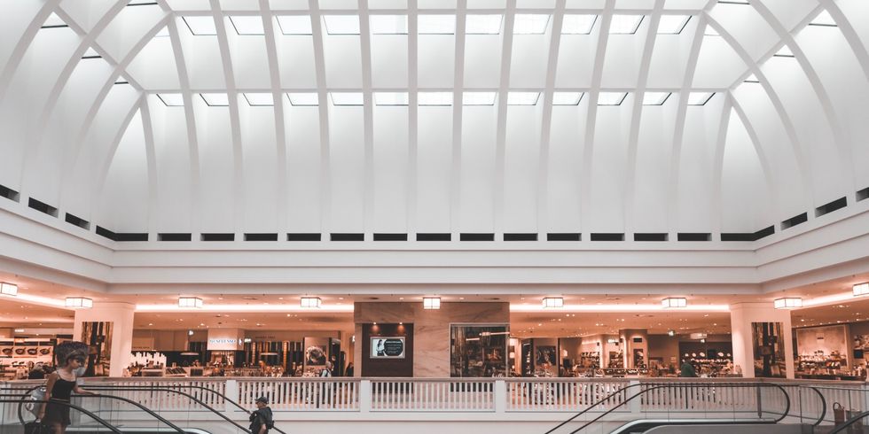 Innenaufnahme eines Einkaufszentrums mit einer Rolltreppe und Geschäften verteilt auf verschiedenen Ebenen.