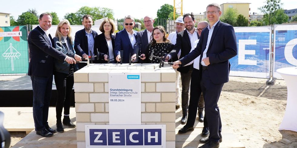 Elf Personen stehen um einen Steinblock mit Hämmern. An dem Steinblock ist ein Schild mit dem Textzug "Grundsteinlegung Integr. Sekundarschule Eisenacher Straße 08.05.2024".