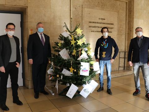 Ein mit gelben Sternen, auf denen Wünsche stehen, geschmückter Weihnachtsbaum und vier Personen