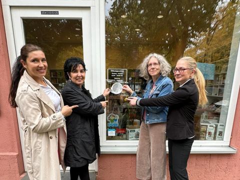 v.l. Einsamkeits und Ehrenamtsbeauftrage Katharina Schulz, Bezirksbürgermeisterin Emine Demirbüken-Wegner, Heike Kornfeld und Rivkah Netzer Geschäftsführerinnen der Buchhandlung am Fellbacher Platz beim Anbringen des Stickers gegen Einsamkeit