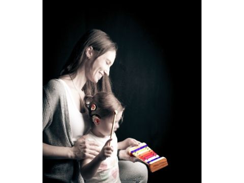 Eine Frau kniet, davor ein Kind, dass ein kleines Xylophone schlägt