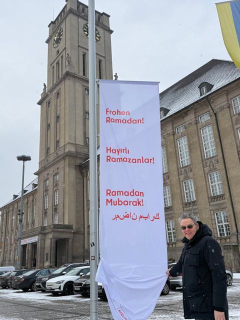 Bezirksbürgermeister Jörn Oltmann hisst die Flagge mit dem Wunsch „Frohen Ramadan“ auf Deutsch, Türkisch und Arabisch.