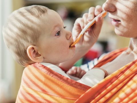Mutter füttert ihr Kind im Tragetuch, das sie am Körper trägt