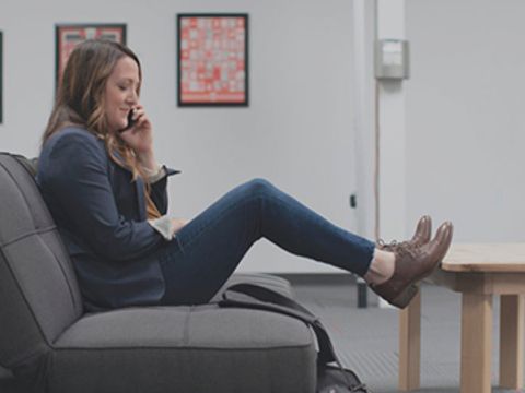 Frau sitzt auf einem Sofa und telefoniert mit den Beinen gegen einen Tisch gelehnt