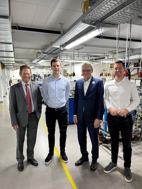 Vier Männer stehen in einer Produktionshalle und lächeln in die Kamera.