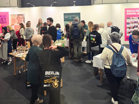 An mehreren Tischen werden verschiedene kulinarische Produkte angeboten, circa 20 Menschen stehen um die Tische