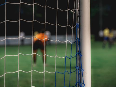 Perspektive hinter dem Tor mit Torwart und weiteren Feldspielern verschwommen im Hintergrund.