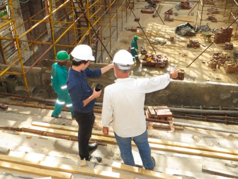 Zwei Arbeiter befinden sich auf einer Baustelle, stehen auf einem Gerüst und beraten sich.