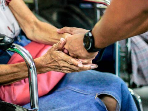 Mann hält Hand mit Frau im Rollstuhl