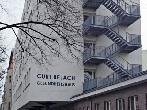 Mehrstöckiges Gebäude mit außenliegender Treppe und Schriftzug 'CURT BEJACH GESUNDHEITSHAUS' an der Fassade