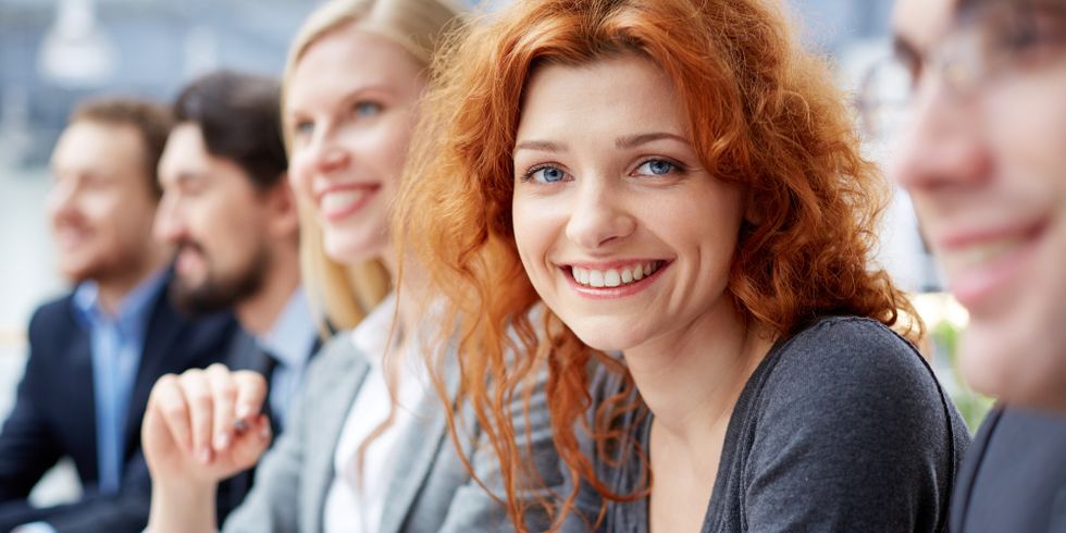 Lächelnde junge Frau sitzt mit vier weiteren lächelnden Menschen an einem Konferenztisch