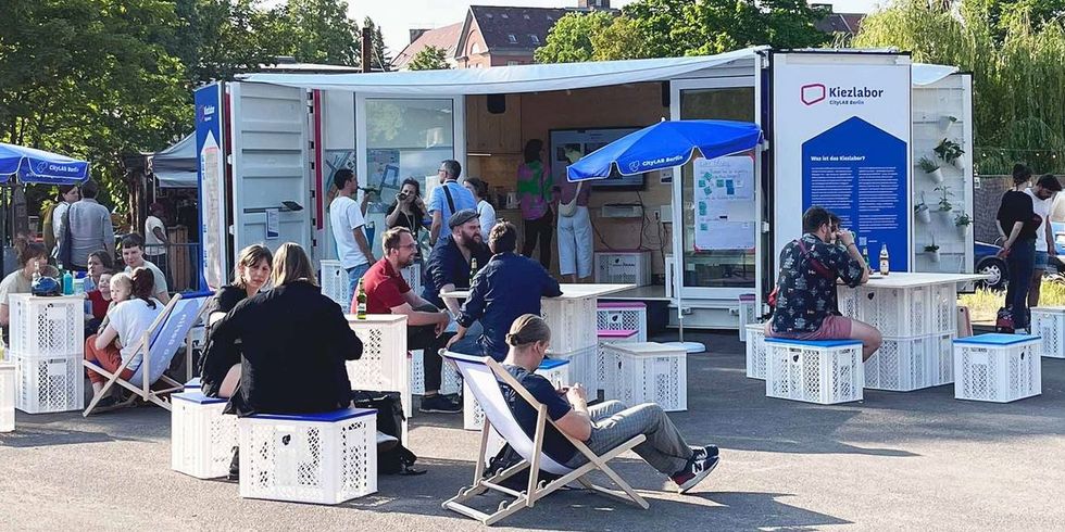 Kiezlabor: umgebauter Schiffscontainer im Hintergrund - Menschen sitzen davor und tauschen sich aus