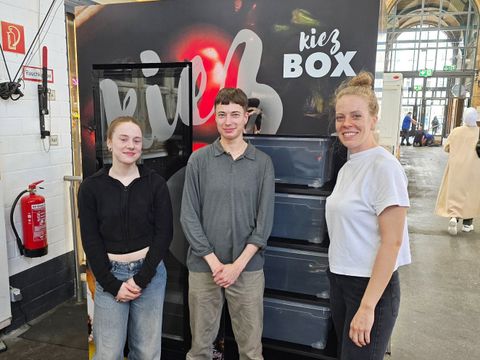 Drei Personen stehen vor der sog. Kiezbox, einem großen Kühlschrank für Lebensmittelrettung