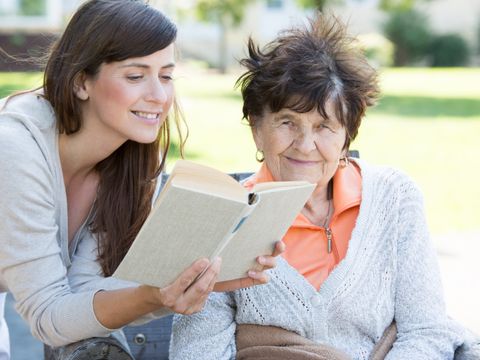 Junge Frau liest Senioren aus einem Buch vor
