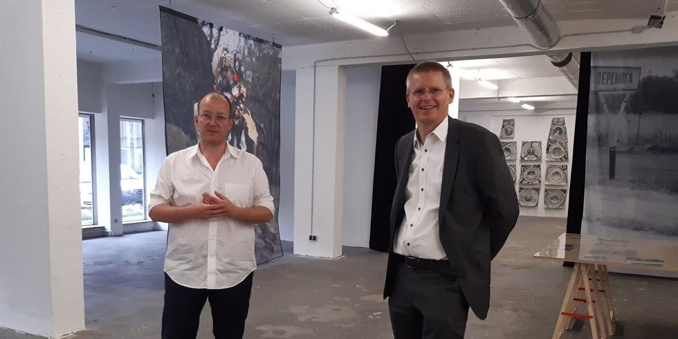 Zwei Männer stehen in einer Halle mit aufgehängten Kunstwerken.