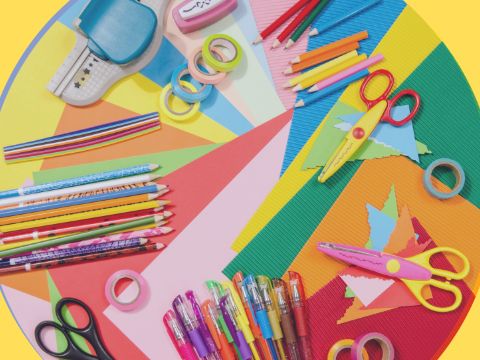 verschiedene bunte Stifte und andere Bastelutensilien liegen auf bunten Bastelpapier