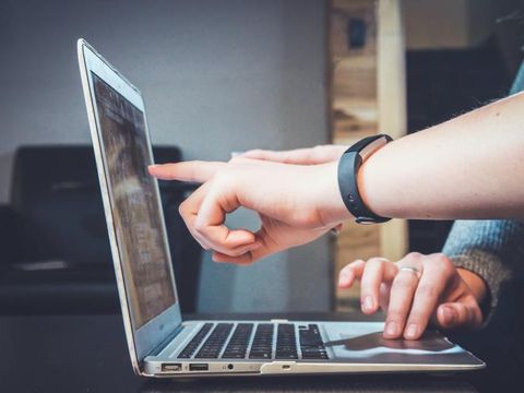 Finger zeigt auf Laptop-Bildschirm, andere Hand liegt auf dem Touchpad