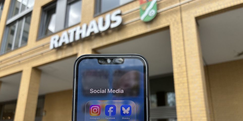 Eine Hand hält ein Smartphone vor dem Bezirksamt Marzahn-Hellersdorf.