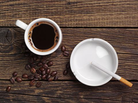 Kaffeetasse und Aschenbecher mit Zigarette stehen auf einem Tisch