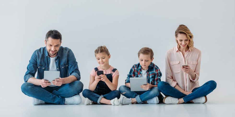 Eltern mit zwei Kindern sitzen auf dem Boden und halten jeweils ein Handy oder ein Tablet