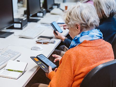 Kursszene - eine ältere Frau mit dem Smartphone in der Hand, sitzend im Computerraum