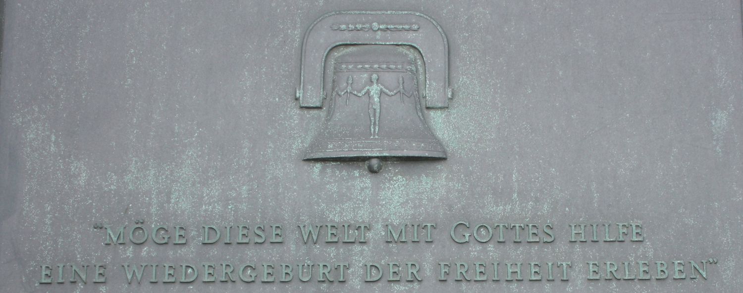 Das Relief einer Glocke mit dem Satz "Möge diese Welt mit Gottes Hilfe eine Wiedergeburt der Freiheit erleben" darunter
