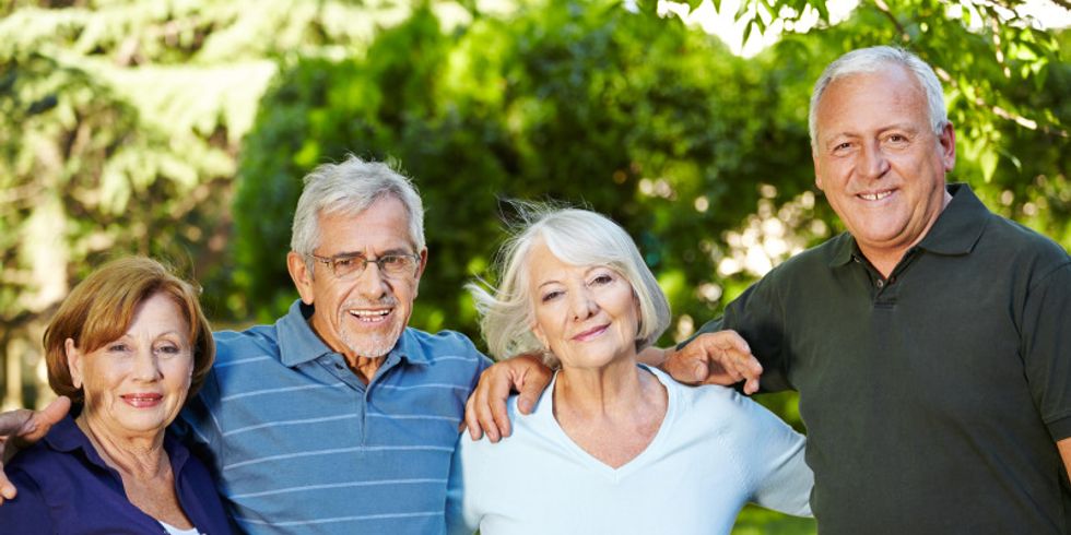 Zwei Seniorinnen und zwei Senioren stehen nah beieinander in einem Park und lächeln in die Kamera