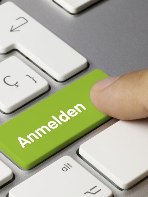 Ein Finger drückt auf eine grüne Taste an einer Tastatur. Auf der Taste steht: Anmelden.