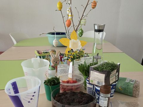 Messbecher, Rezepte, Kräuter und Tomaten Tomaten liegen mit weiteren Lebensmitteln und Osterdekoration auf einem Tisch