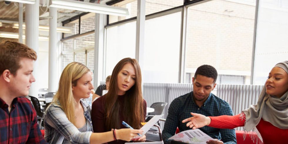 Gruppe Studenten sitzt an einem runden Tisch und macht Projektarbeit