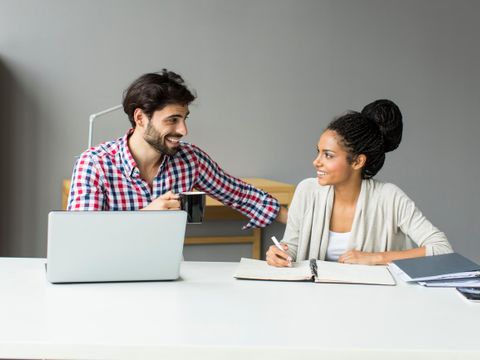 Zwei Personen sprechen am Schreibtisch und machen digitale und analoge Notizen.
