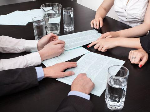 Verschiedene Schriftstücke liegen auf einem Tisch und werden von mehreren Personen diskutiert