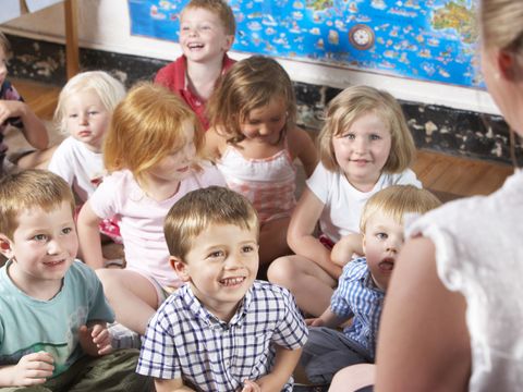 Kinder sitzen im Kindergarten auf dem Boden und hören Erzieherin zu