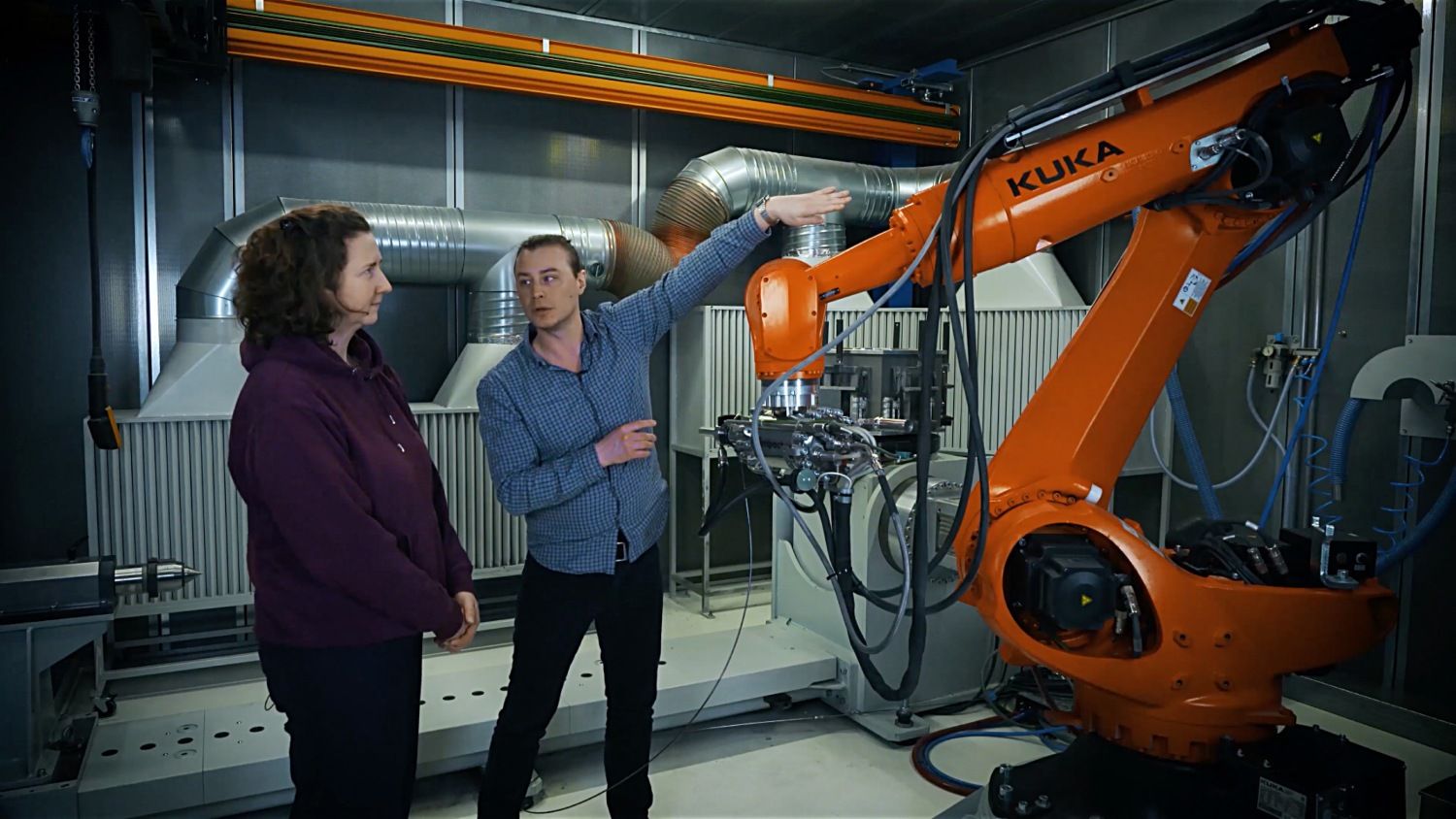 Ein Mann und eine Frau stehen an einem orangenen Roboterarm