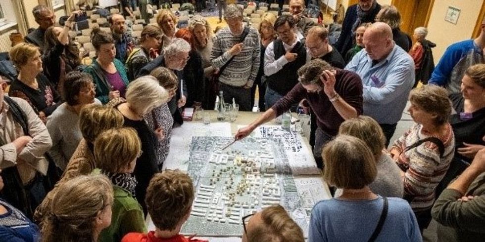 Viele Menschen stehen an einem Tisch, auf dem ein großer Straßenplan liegt