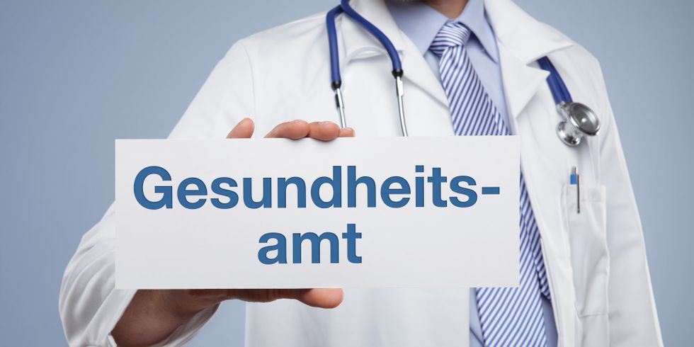 Arzt hält Schild mit der Aufschrift "Gesundheitsamt"