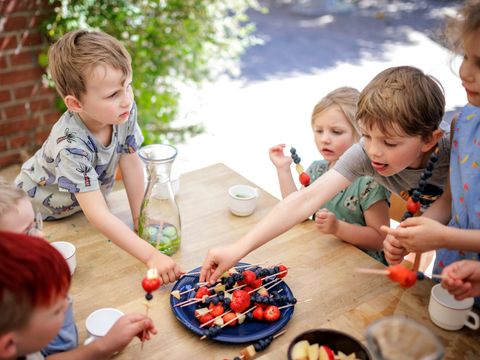 Kinder sitzen an einem Tisch und essen Obstspieße