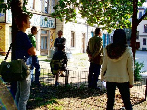 Mehrere Menschen stehen im Schatten zwischen Bäumen.