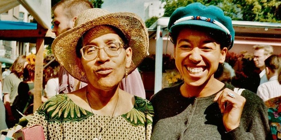 Zwei dunkelhäutige Frauen sind an einem sonnigen Tag draußen und lächeln in die Kamera.