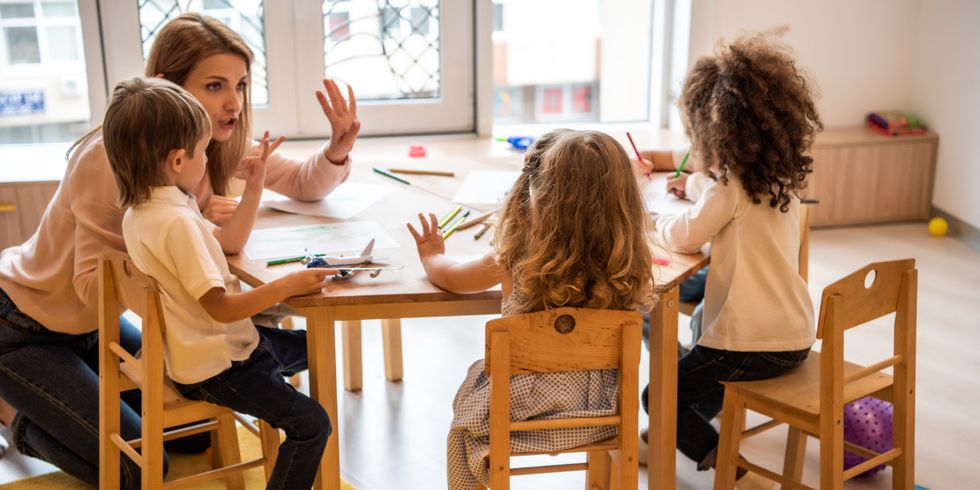 Erzieherin zählt mit kleinen Kindern am Tisch in der Kita