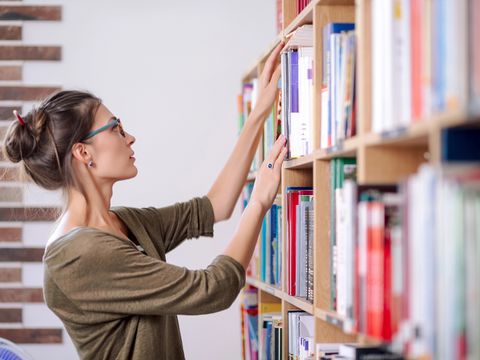 Junge Frau mit Brille auf der Suche nach einem Buch in einem Bücherregal